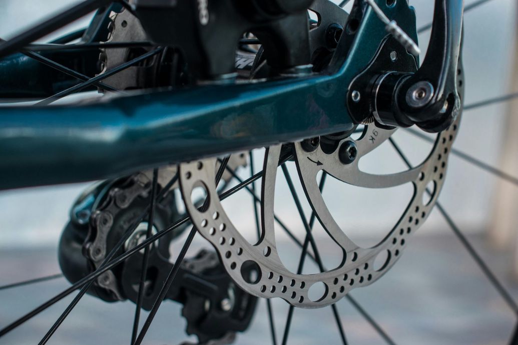 Close-up of a bicycle's rear wheel with a disc brake, showing the rotor, frame, and spokes.