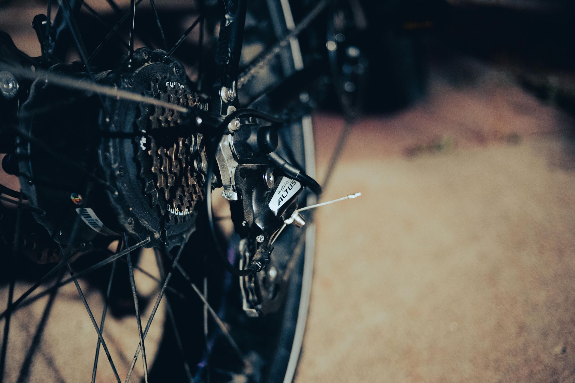 Close-up of bicycle rear wheel, gears, and derailleur. Black components with rusty cassette; on brown surface.